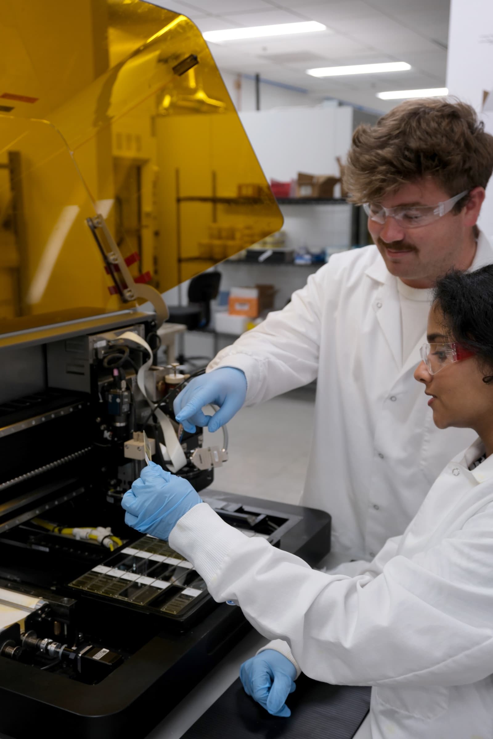 Two lab scientists in coats and safety glasses loading a tissue slide into the QCPRECISE instrument